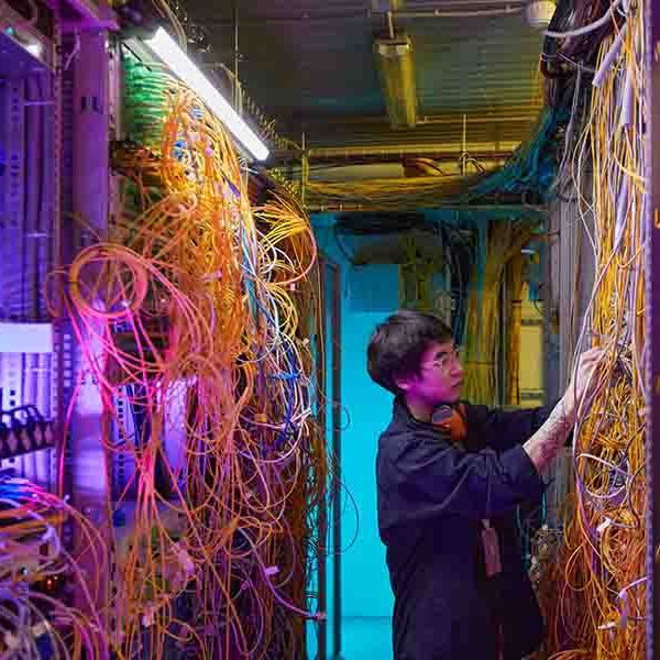 Technician Inspecting Server Hub Wide angle side view at young network technician connecting wires and cables in server room, copy space